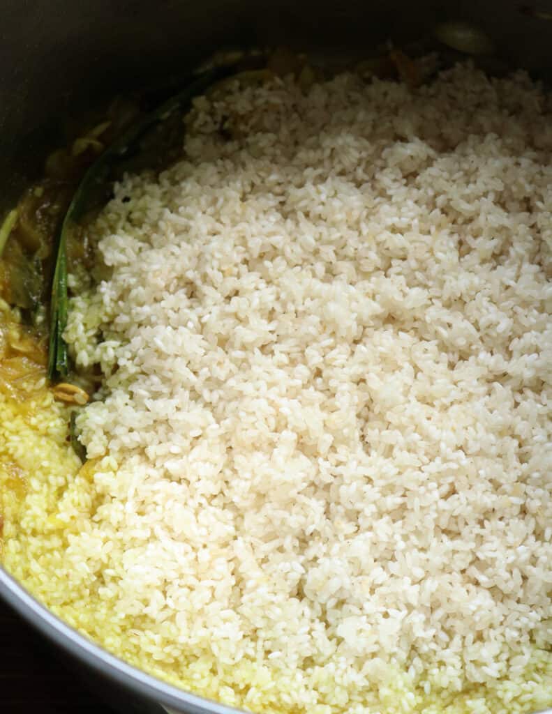 adding the washed rice to the tempered oil, onions, pandan and spices.