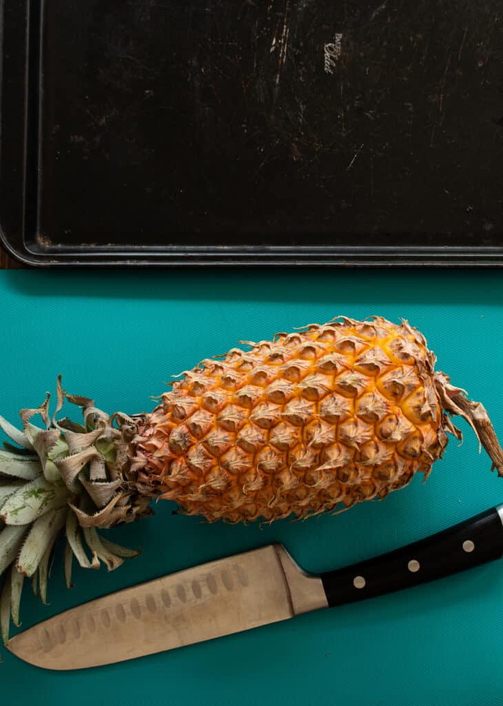 whole pineapple with a black platter and a knife ready to be cut.