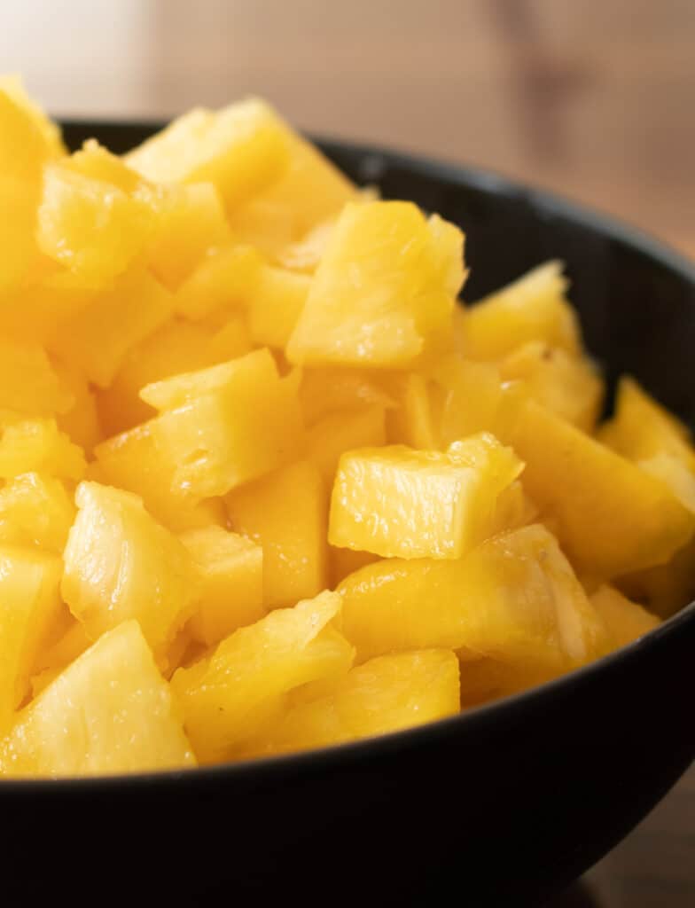 cubed pineapple placed into a cube into a black bowl to make the pineapple chutney.