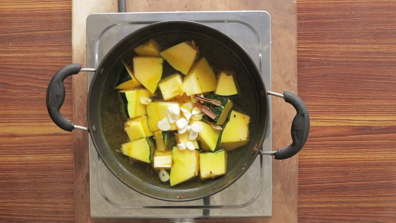 adding garlic, and the aromatic spices to the pan to cook the pumpkin curry.