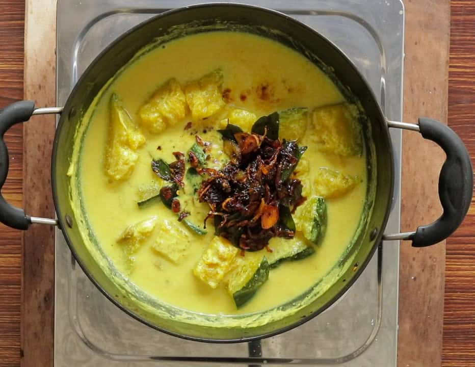 adding the tempered ingredients into the cooking pumpkin curry.