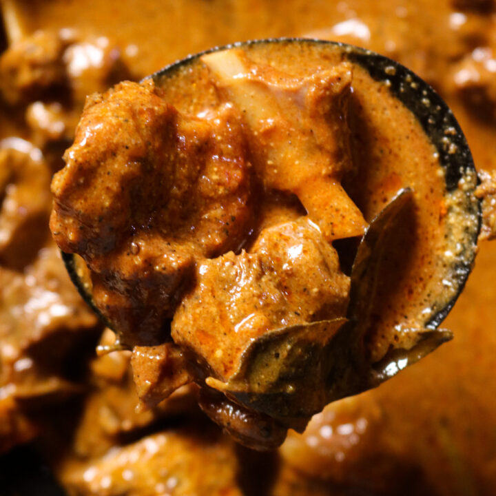 mutton curry served with a wooden spoon.