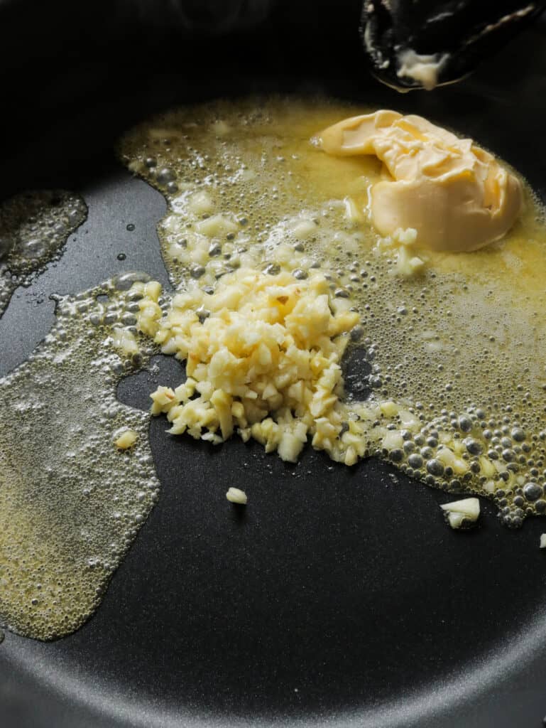 adding minced ginger and garlic to the melting butter in the large frying pan.