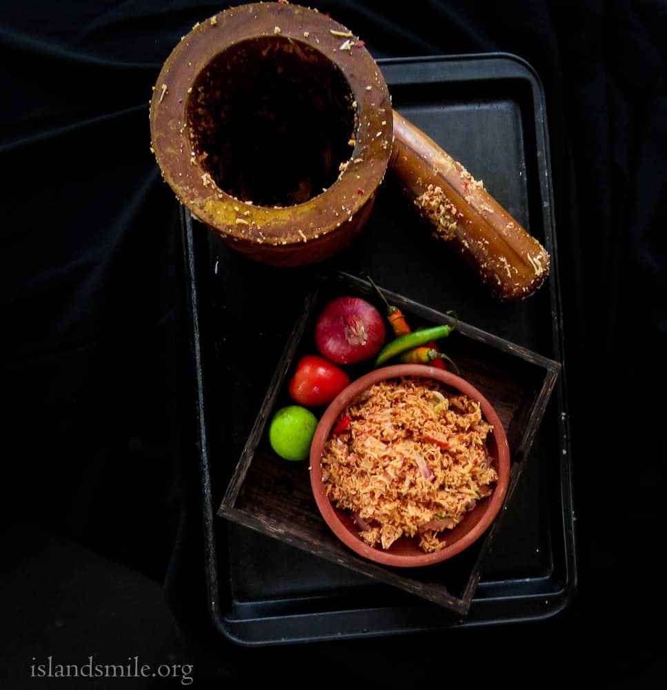 pol sambol in a clay pot with onions, tomatoes, lime , green chillies and a mortar and pestle on a black tray