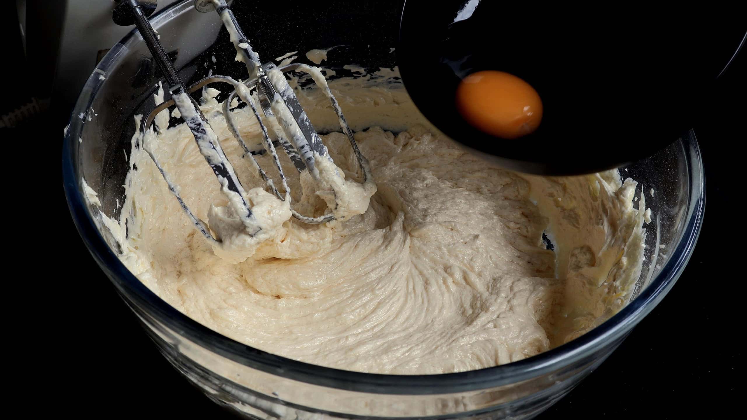 adding eggs one at a time to the batter.