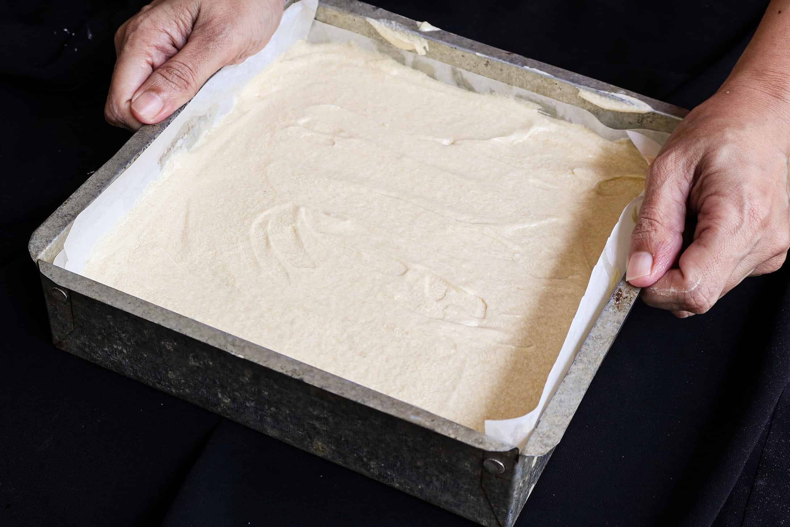adding the butter cake batter to the cake pan.
