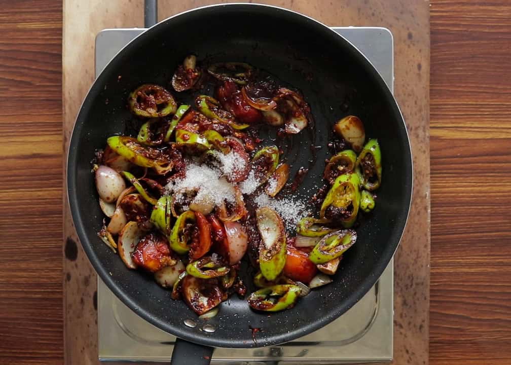 adding sugar to the stir frying ingredients for the devilled chicken.