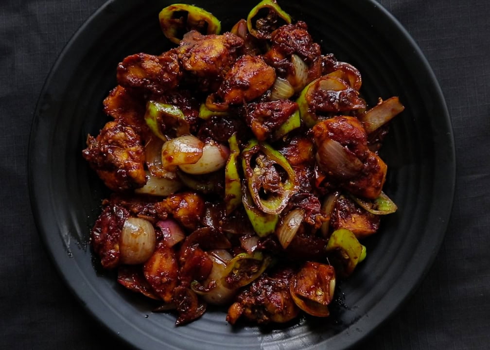 devilled chicken served on a blacl platter.