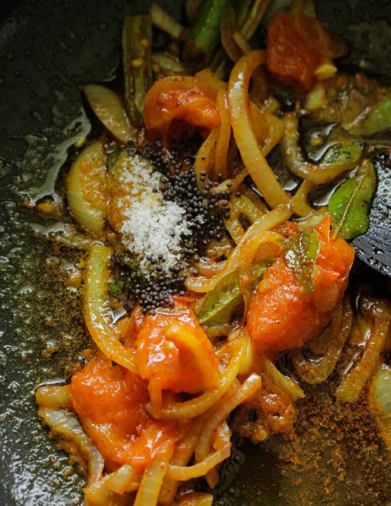 adding mustard seeds and salt to cooking tomatoes and onions in the pan.