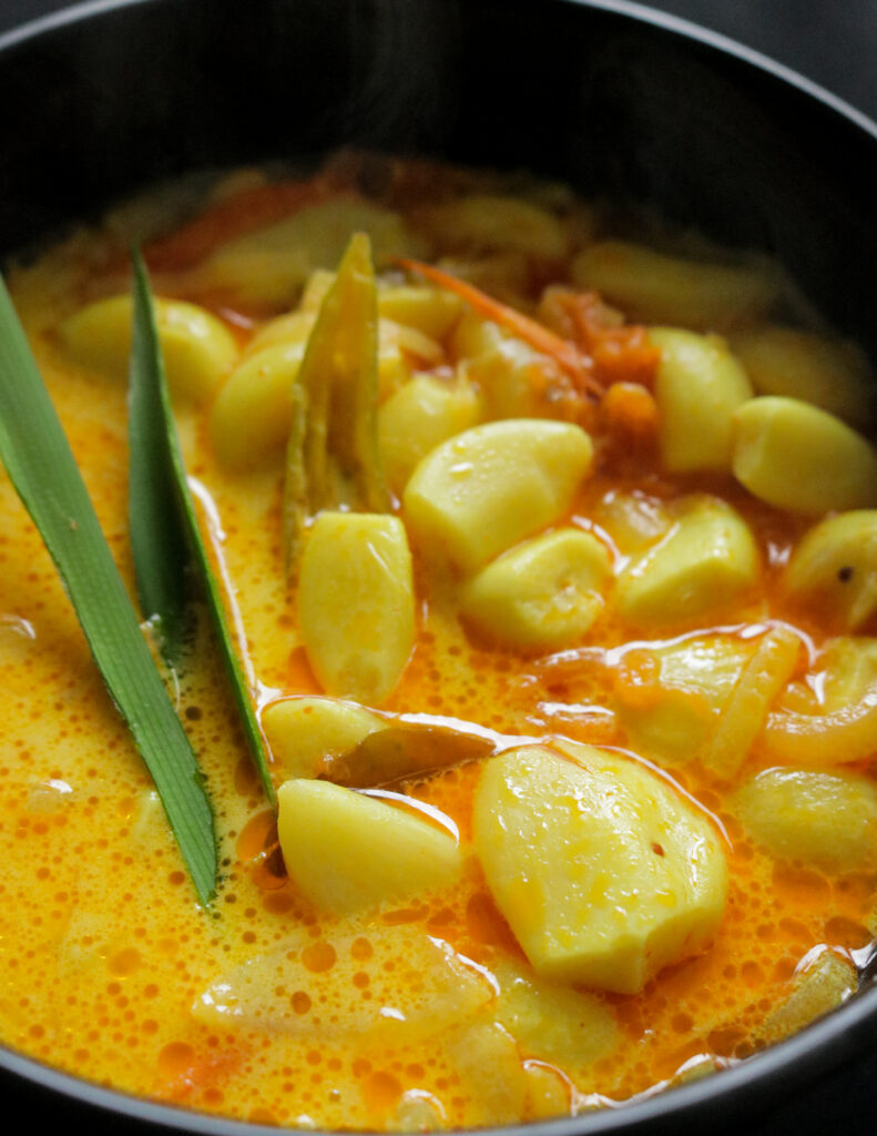 Garlic curry served in a black bowl with pandan leaf to garnish.