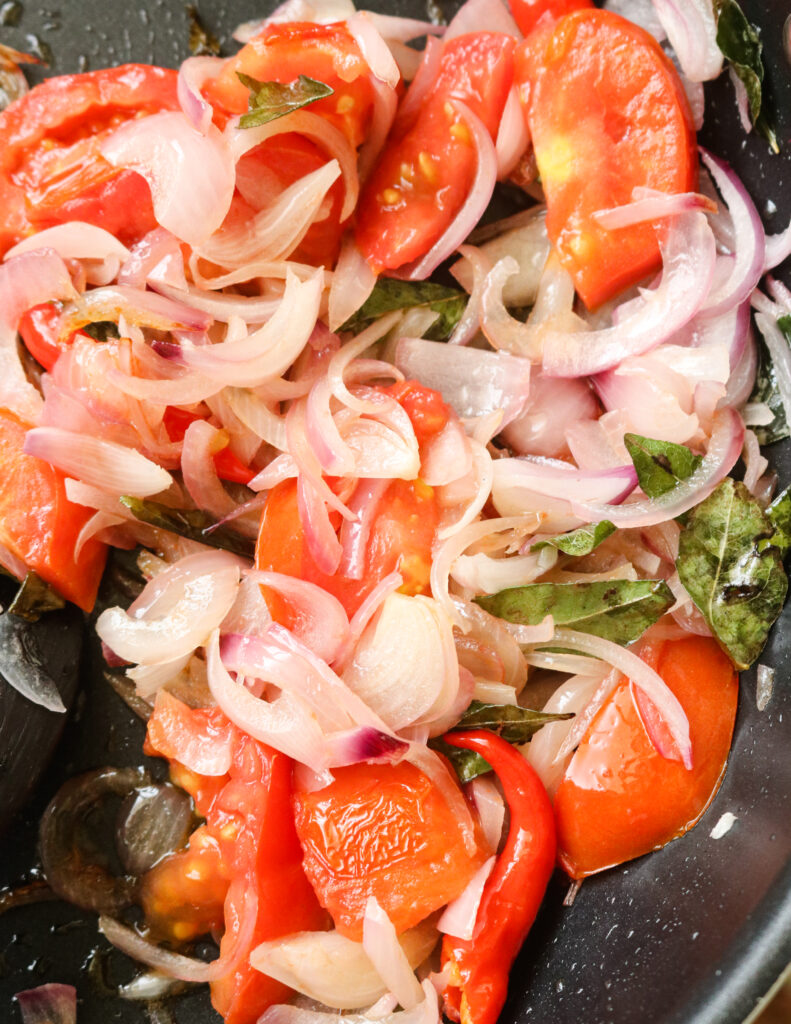 cooked tomatoes, onions, curry leaves cooked in a pan.