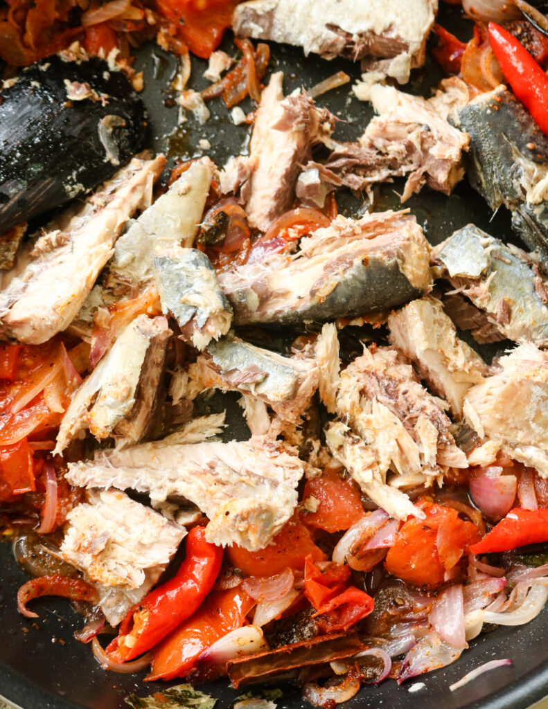 canned mackerel added to the tomatoes, red chillies, onion cooked in the pan with a wooden spoon.