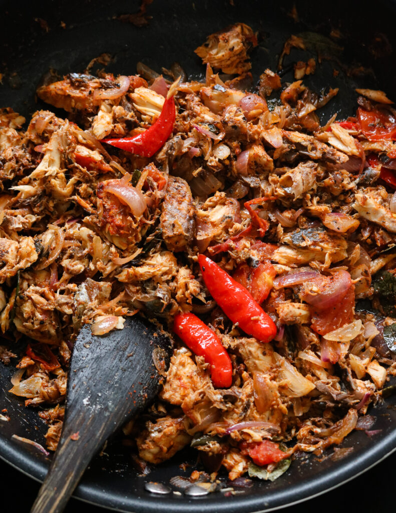 canned mackerel stir fry cooked in a pan with red chillies and a wooden spoon in the pan.