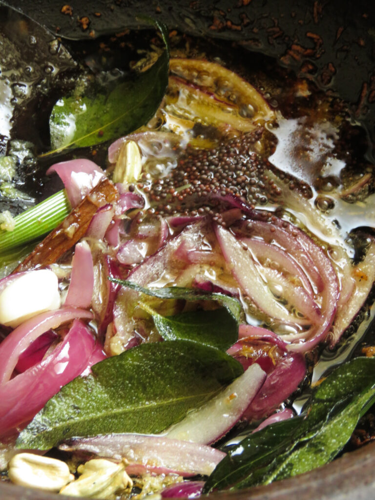 adding onions, cardamom, cinnamon, and mustard to cook the baby jackfruit curry.