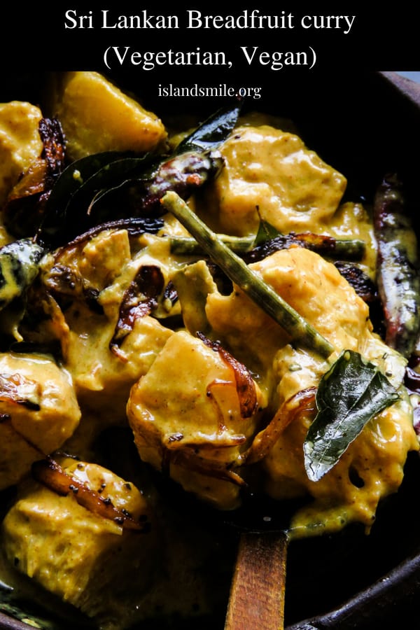 Sri Lankan breadfruit curry scooped with a wooden spoon and garnished with tempered curry leaves and onions.