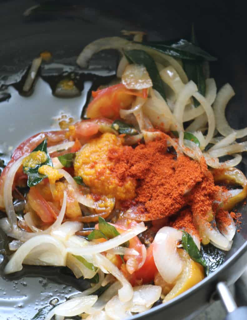 adding spice powders to the cooking onions and tomatoes tempering to cook chicken chettinad.