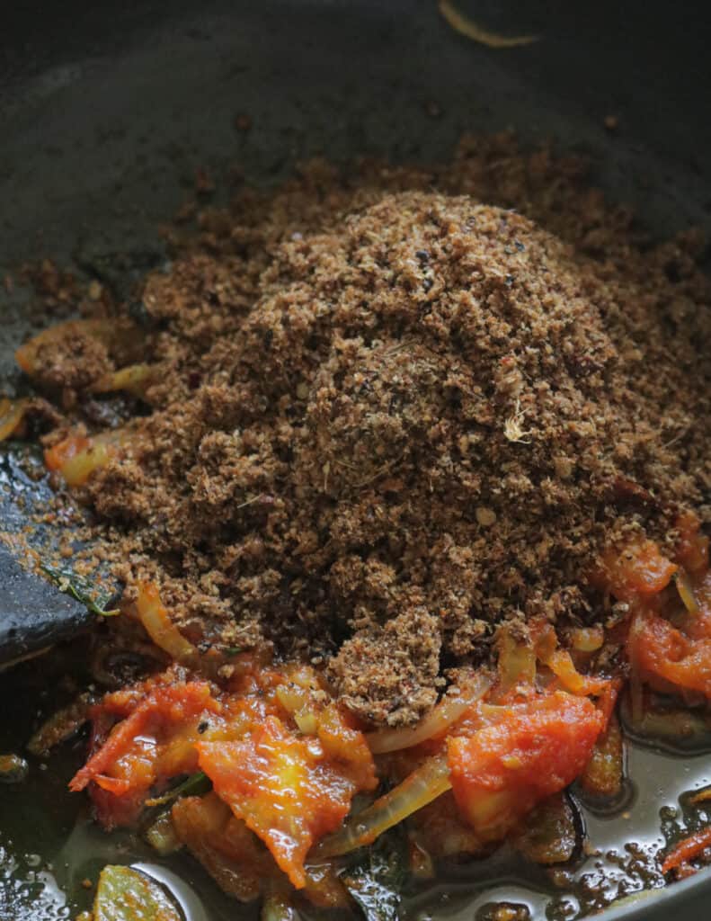 adding the spice powder to the cooking ingredients to make the chettinad chicken.