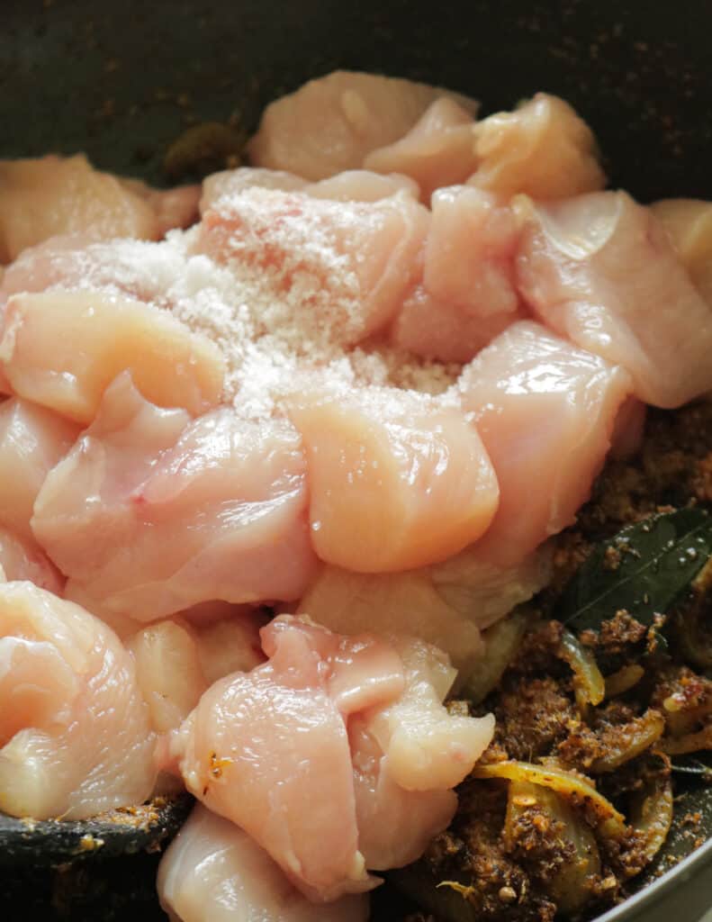 adding the chicken cubes and salt to cook the chettinad chicken.