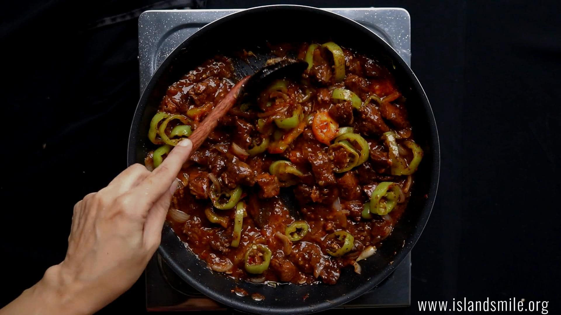 devilled beef cooking over a stove top and stirring with a wooden spoon.