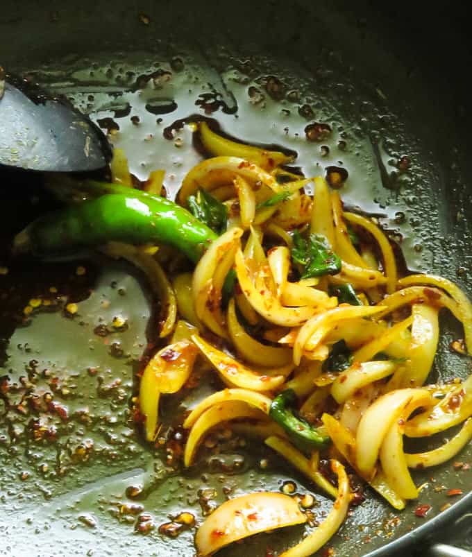 tempering the onions in a pan to make the banana blossom recipe.