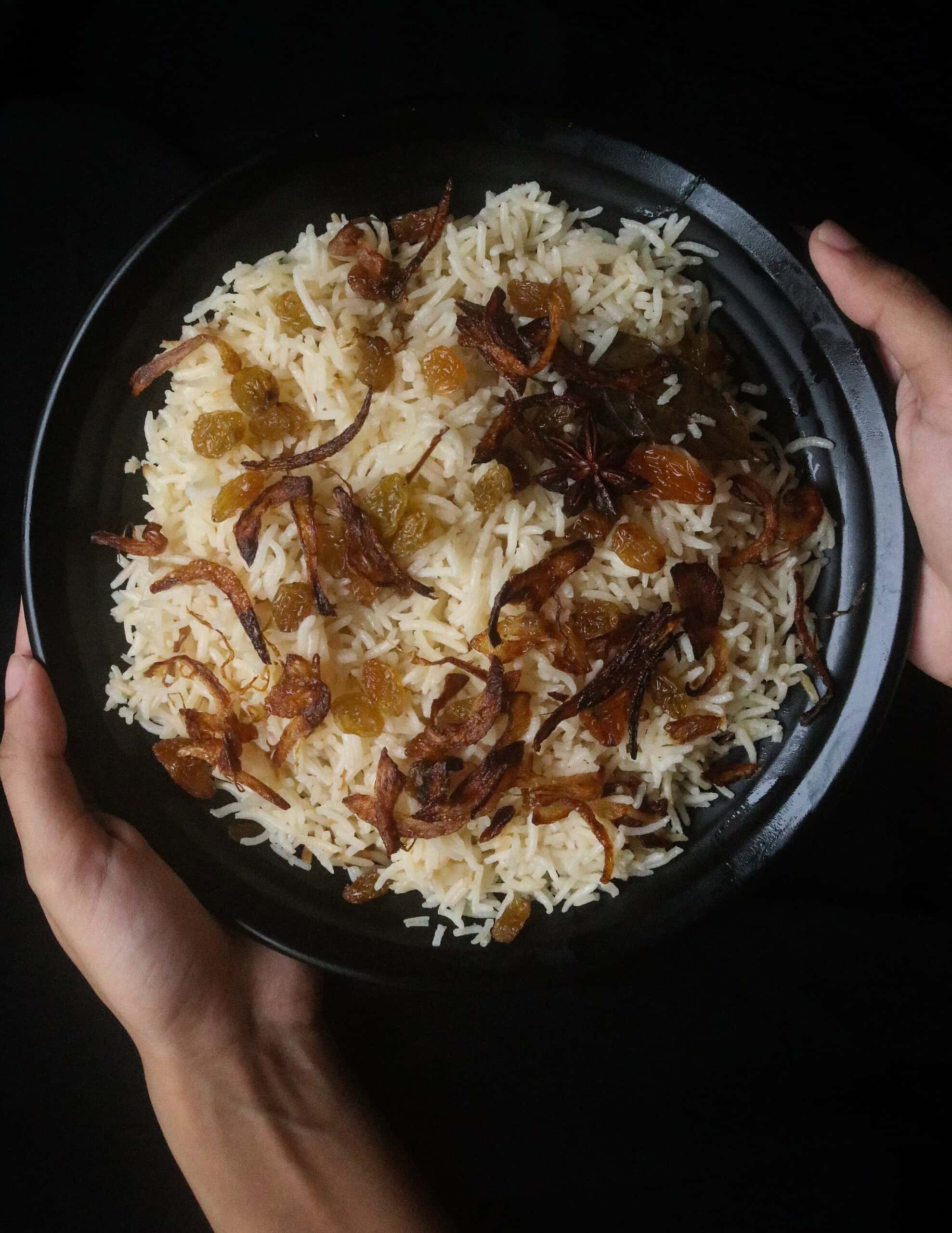 ghee rice served in a black plate fried onions and fried raisins.