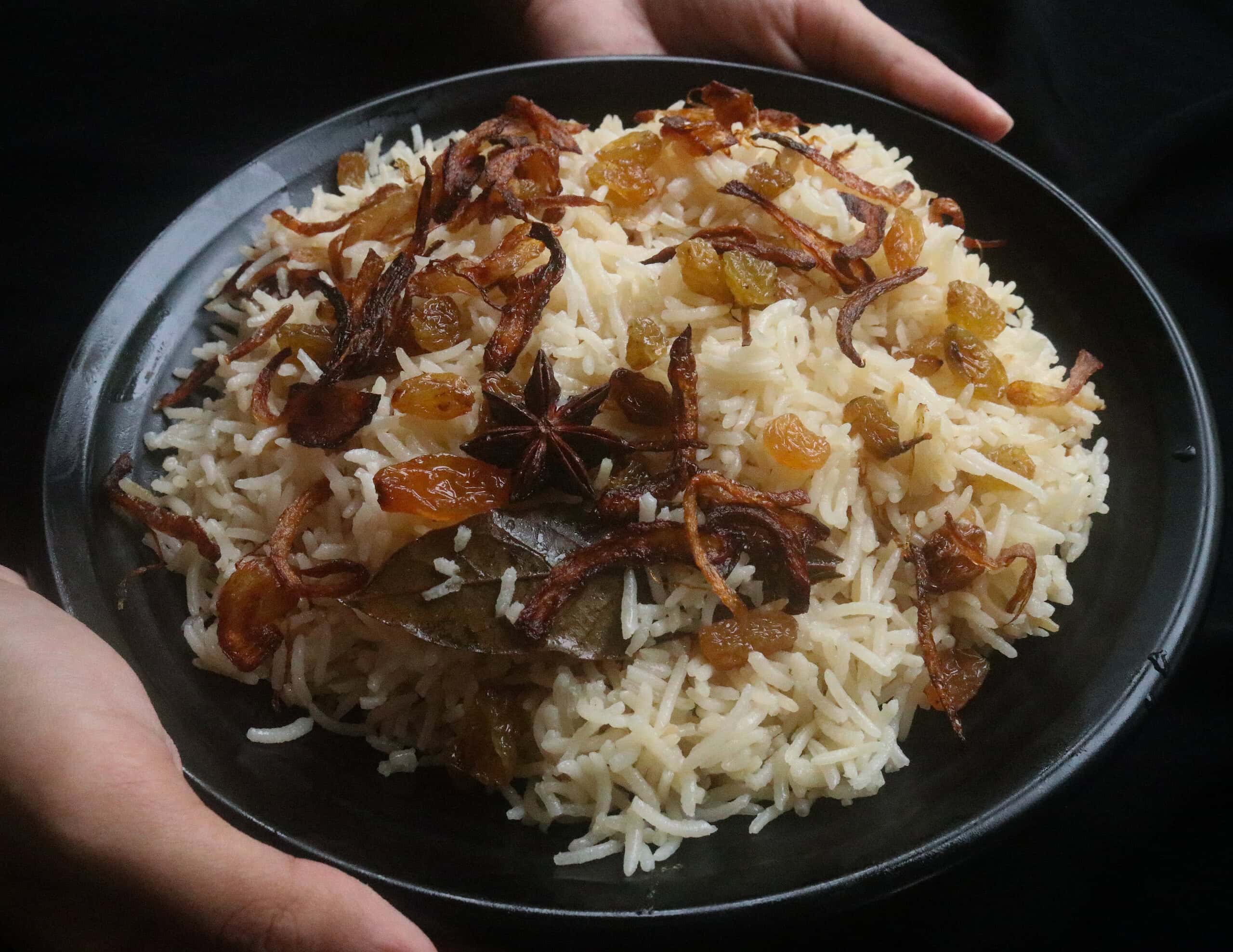 serving ghee rice on a platter with raisins and fried onions and aromatics.