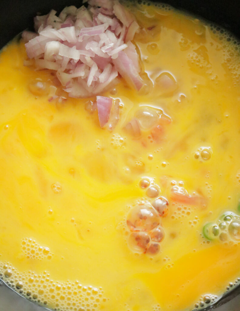 adding whiked eggs to the ingredients to make omelette