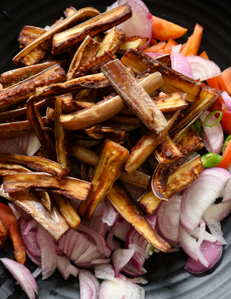 mixing the fried eggplant strips with the onions and tomatoes