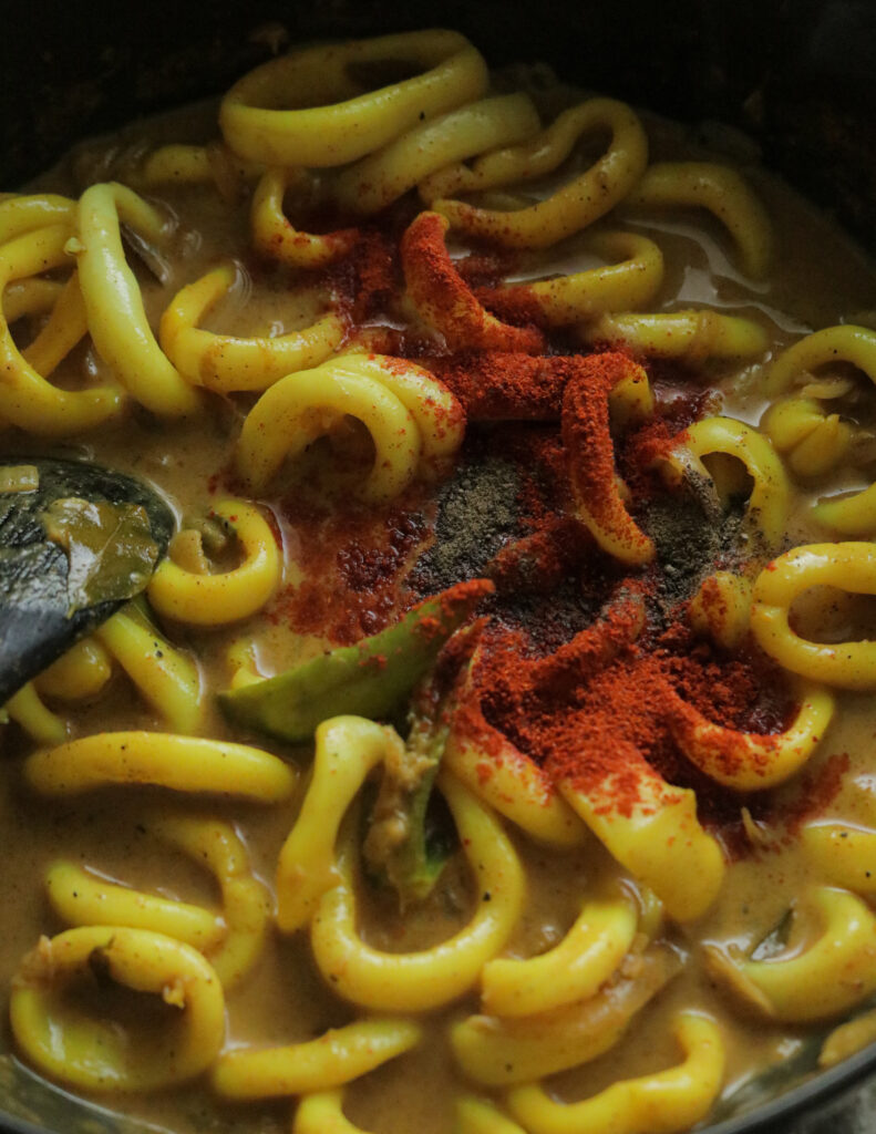 adding spices to the calamari curry that is cooking.