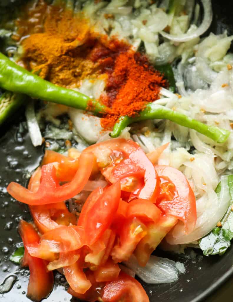 cooking tomatoes, red chilli powder, turmeric powder and green chilli to make the fish curry