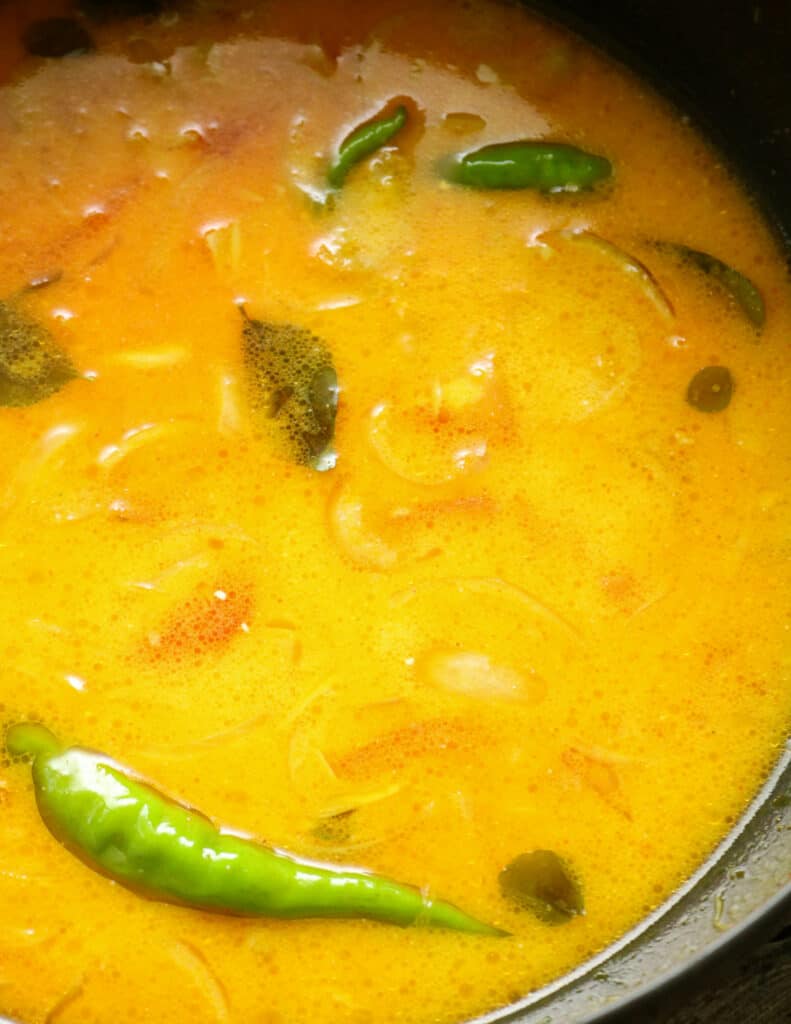 adding coconut milk to the tempered ingredients to make the fish curry.