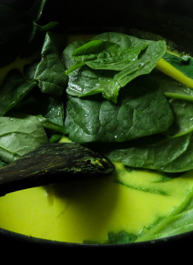 adding spinach to the coconut milk gravy.