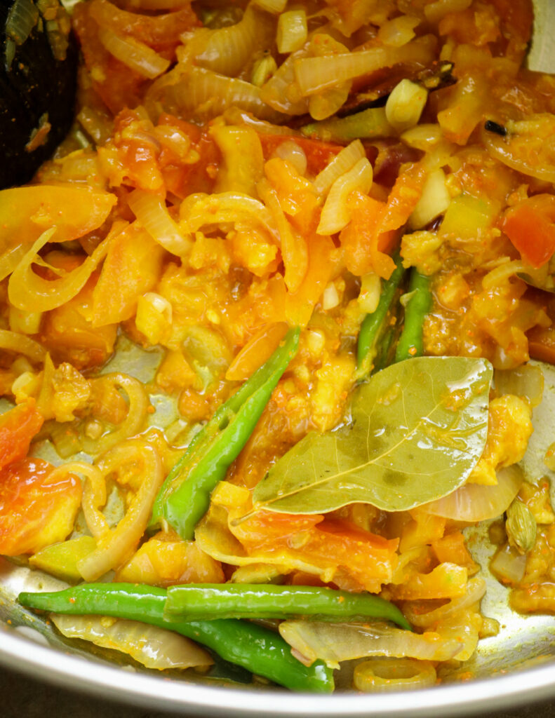 adding chopped tomato to the cooked onions and bay leaves, green chillies in a pan.