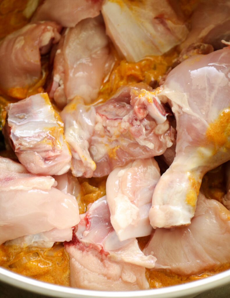 adding chicken parts to the chopped tomato, yoghurt and cooked onions, spices.