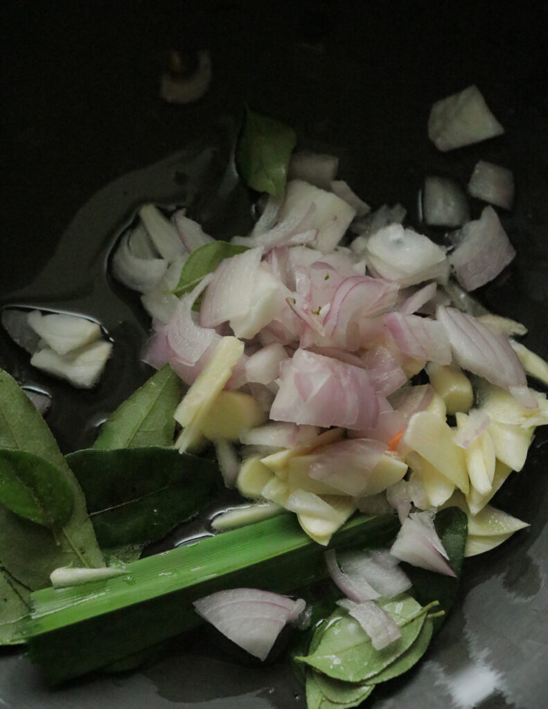 cooking the sliced onions, sliced garlic, curry leaves in oil in a pot to make carrot curry.