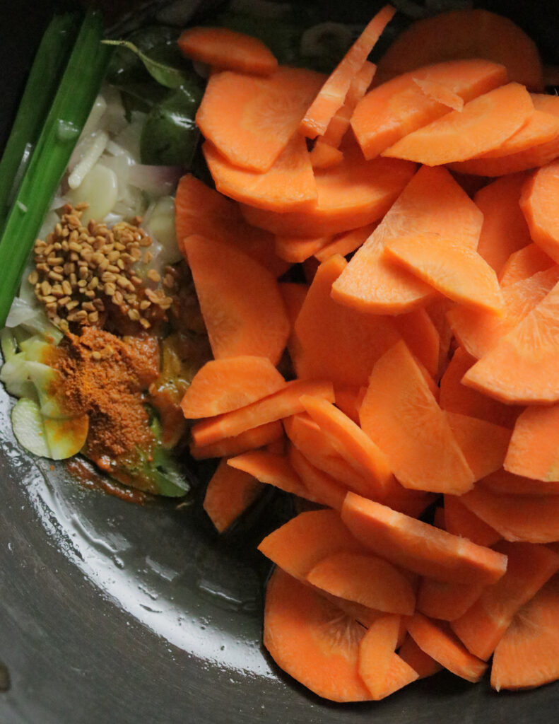 adding sliced carrot, fenugrrel seeds, garlic, pandan leaves and onions to cook carrot curry.