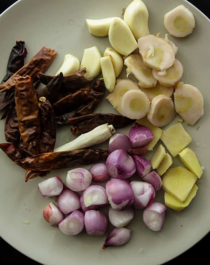 dried red chilies, ginger, galangal, lemongrass,  shallots, garlic. the ingredients to make rendang on a plate.
