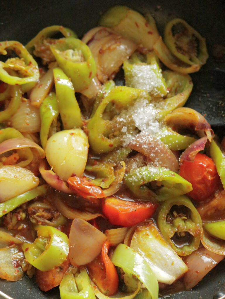 adding sugar to the wedges of green peppers and onions to make the devilled sausages