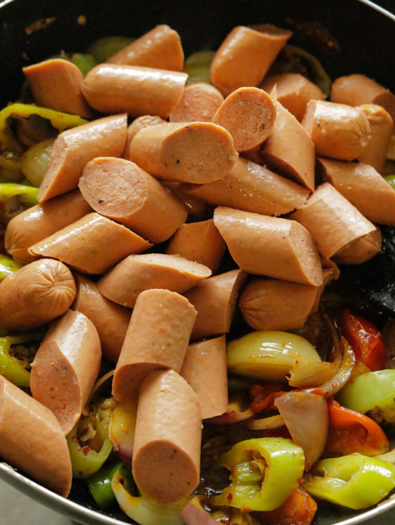 adding the sliced sausages to the tomatoes, green peppers and wedges of onions 