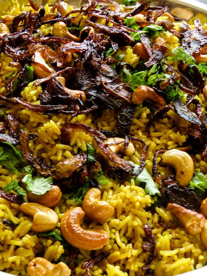 adding the caramelized onions and fried cashews, coriander leaves over the egg biryani rice.