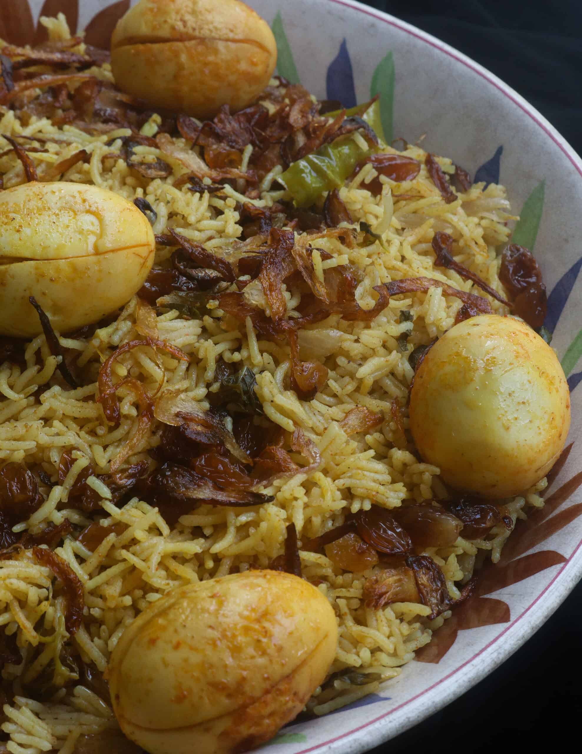 egg biryani layered with fried onions, raisins and fried eggs served on a large platter.