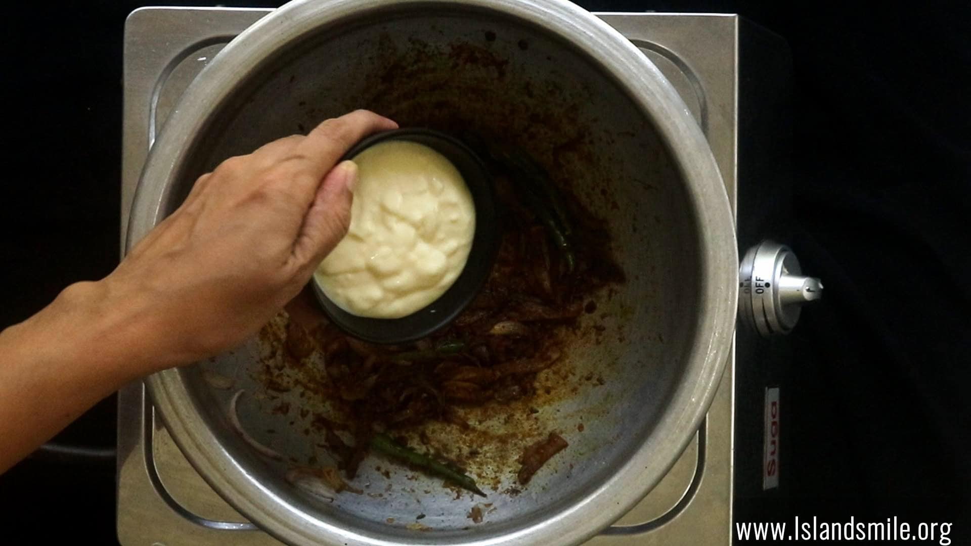 adding the yoghurt to the spices to the pan cooking the egg biryani.