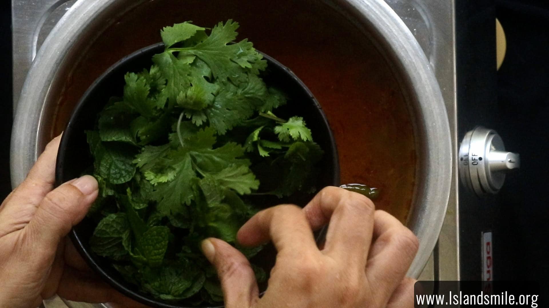 adding the coriander leaves and mint leaves to cook the egg biryani.
