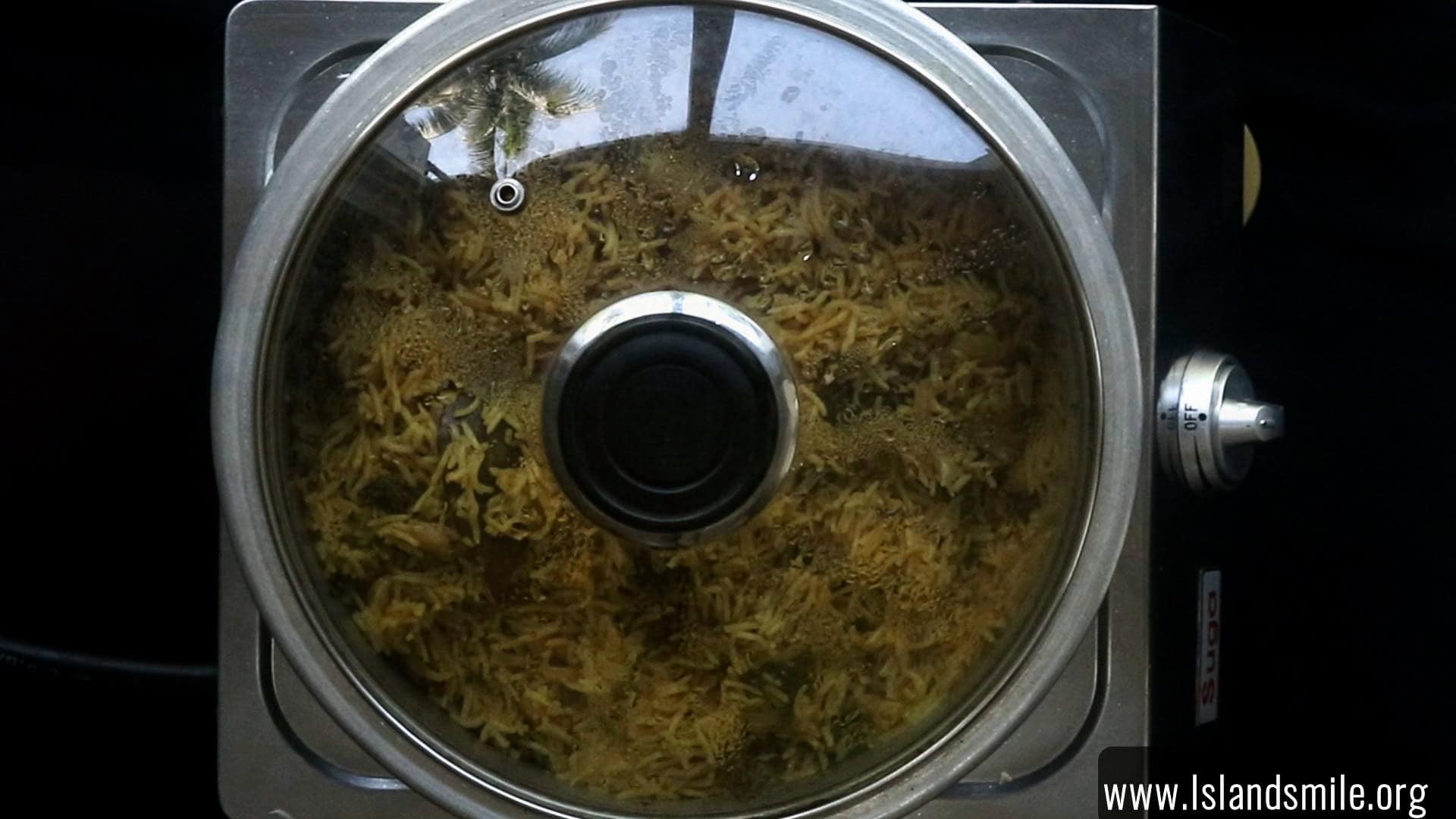 cooking the egg biryani in a wide mouthed pan with a glass lid.