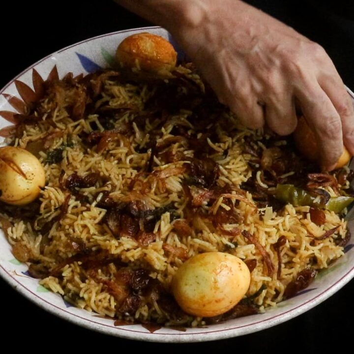 egg biryani with egg placed on the rice with onion and raisins garnishing.
