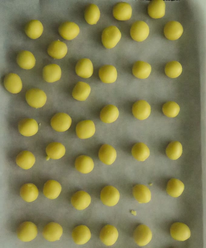 formed balls placed on a tray covered in parchment paper then covered.