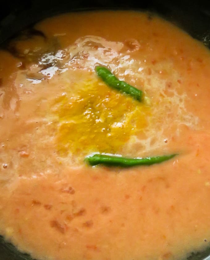 cooking the blended tomato base in a pan to thicken with tur,eric and green chillies.