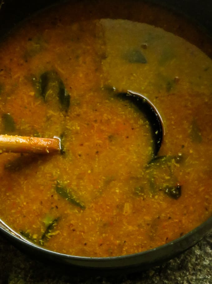 tomato rasam in a cooking pan with a wooden spoon.