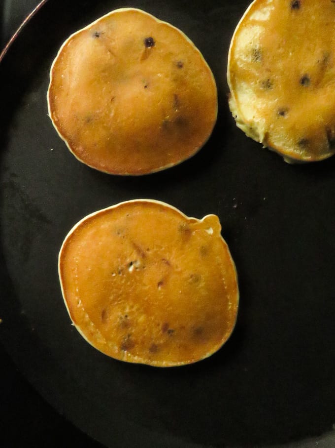 cooking the  banana chocolate chip pancakes in a frying pan.