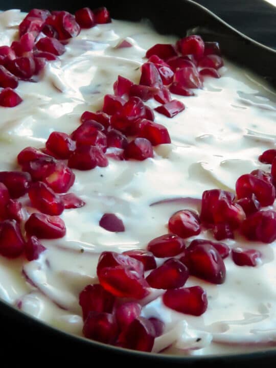 A bowl of onion raita made with yogurt and finely sliced onions and dottd with pomegranates.